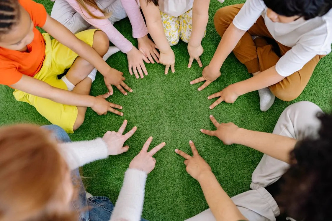 Anak-anak bermain permainan kelompok di lapangan rumput hijau, melatih kerja sama tim.